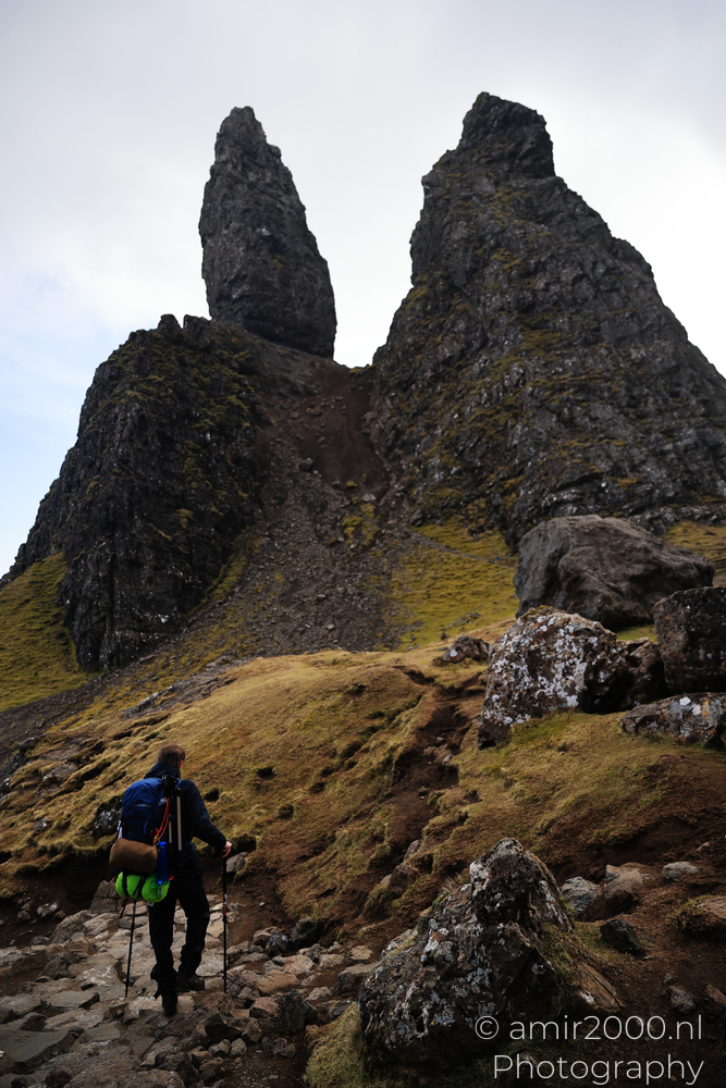 Hiker climbing toward Old Man of Storr rock pinnacles on Isle of Skye