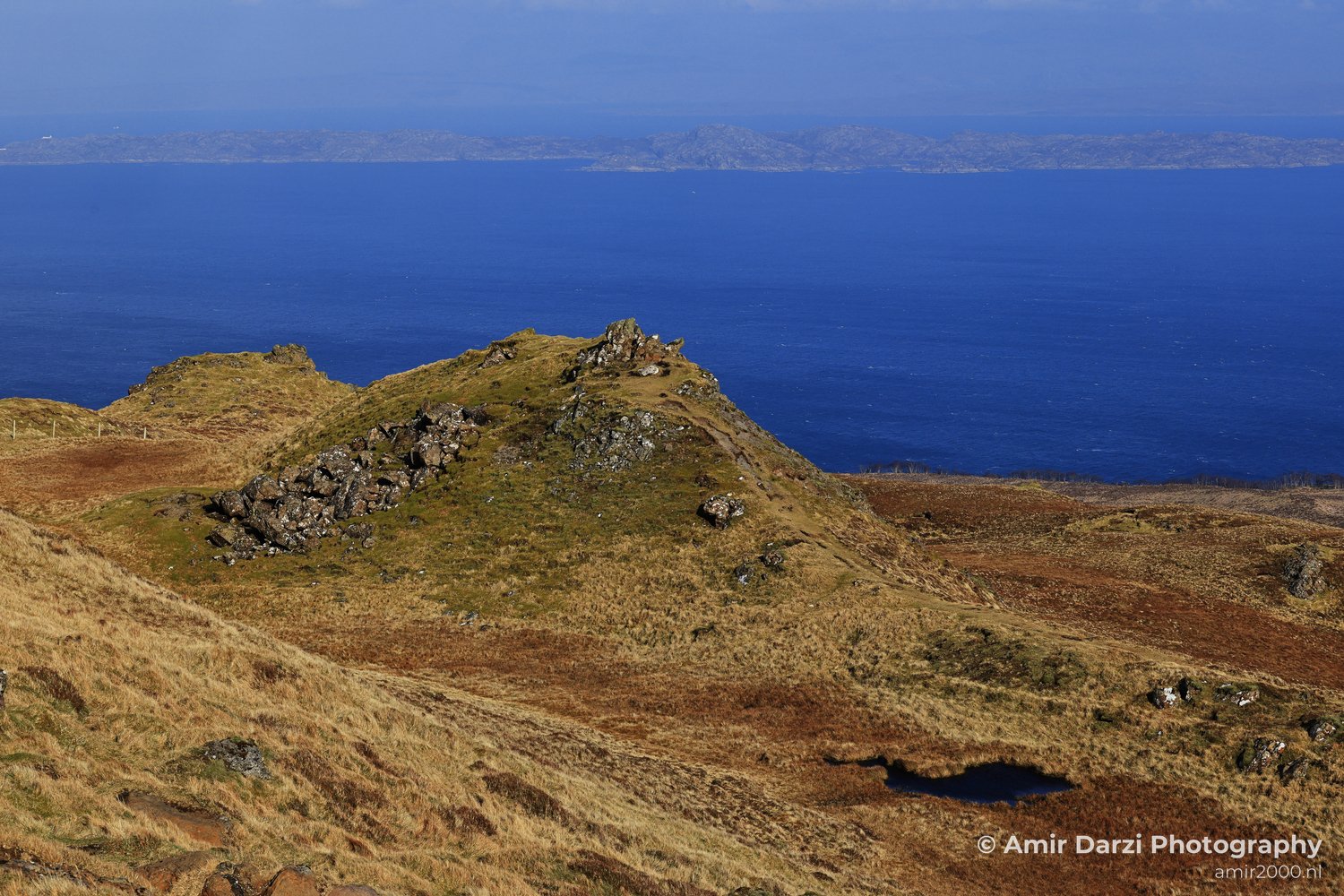 Old Man Storr a scenic view of a rocky hillside overlooking the ocean with distant islands.