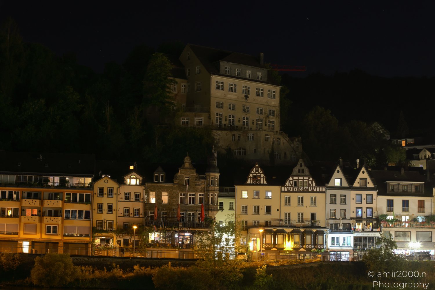 Hillside building rising above illuminated riverside houses in Cochem, Rhineland-Palatinate, Germany