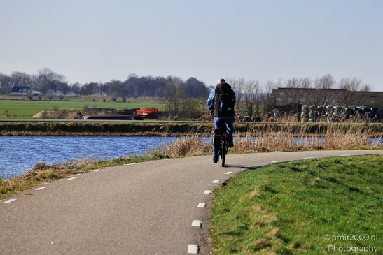 Person riding a bicycle on a paved path near a body of water in Ouderkerk aan de Amstel, - image from year 2026 #002