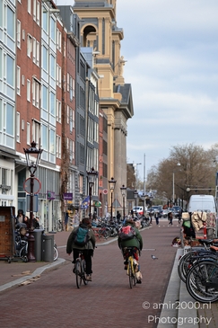 People riding bicycles, parked bikes along the street in Amsterdam, Netherlands. - image from year 2026 #001