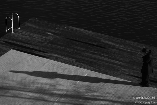 A solitary figure stands on a dock, casting a long shadow against the water. - image from year 2026 #001