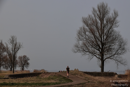 A person appears in the center of the image, walking along a path in Naarden, Netherlands. - image from year 2026 #001