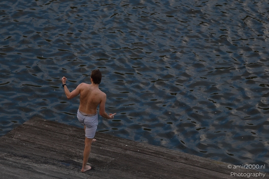 A shirtless man stands on a wooden dock by the waters edge. - image from year 2026 #001