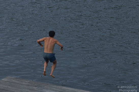 A young man leaps off a dock into calm water in Amsterdam, Netherlands. - image from year 2026 #002
