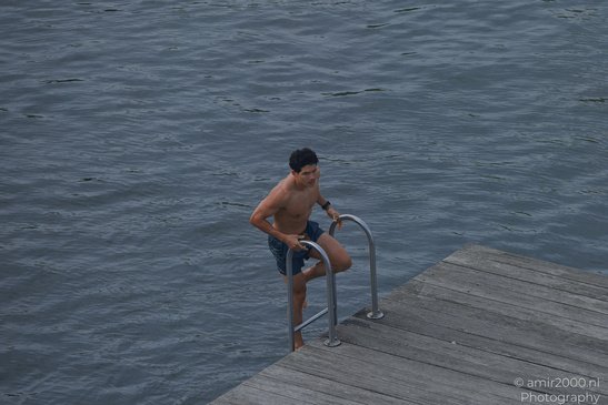 A young man stands on a dock, preparing to jump into the water in Amsterdam, Netherlands. - image from year 2026 #005