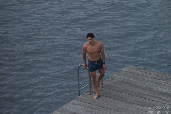 A shirtless man stands on a wooden dock, preparing to jump into the water in Amsterdam, - image from year 2026 #006