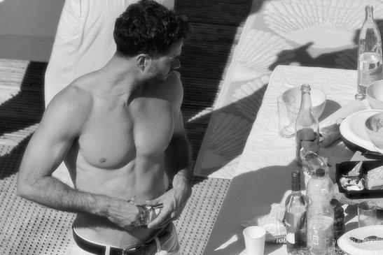 A shirtless individual adjusting their shorts, with a table in the foreground containing various - image from year 2026 #001