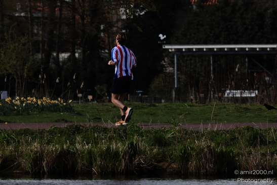 A runner in a striped shirt and black shorts is sprinting along the edge of a lake at dusk. - image from year 2026 #001