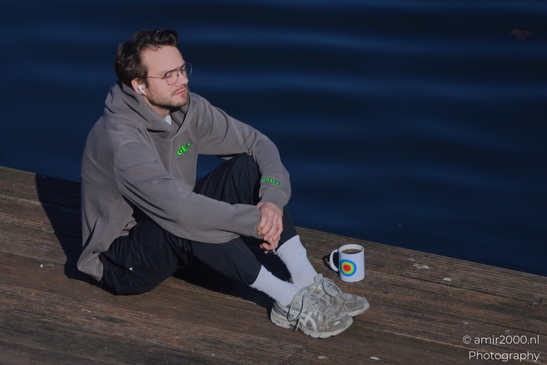 Side view of a man sitting with coffee on a wooden dock beside canal water. - image from year 2026 #002