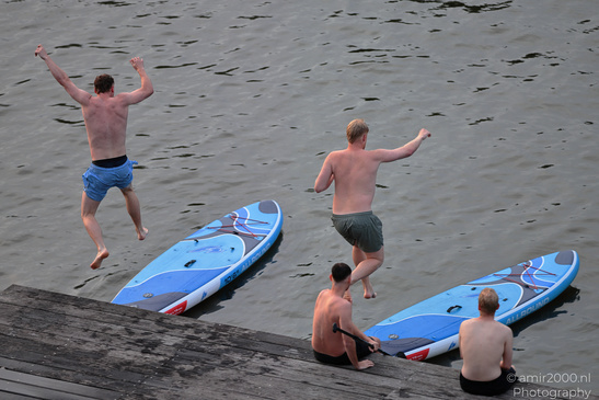 A group of shirtless men are seen leaping into the water from a wooden pier with their paddleboards image from year 2026 #7