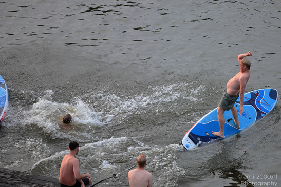 A blue stand-up paddleboard and swimmers are seen in the Amsterdam canal from above. image from year 2026 #13