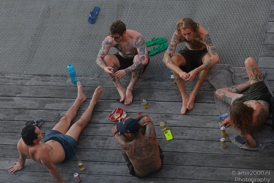 Four tattooed men relax on a wooden dock, enjoying drinks and snacks in Amsterdam, Netherlands. - image from year 2026 #003