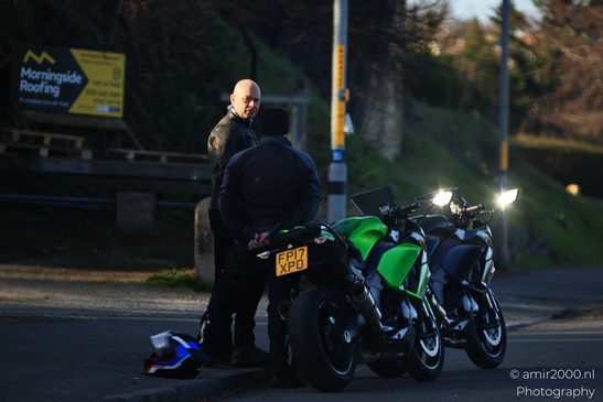 Two motorcyclists stand beside their bikes on a road at dusk. - image from year 2026 #001