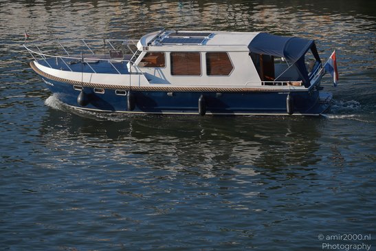 A blue and white houseboat with a solar panel on the roof, a canopy, and flags on either side, - image from year 2026 #008