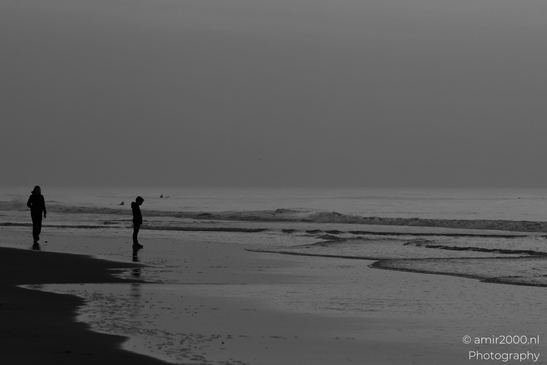 A beach scene at twilight, featuring two people walking and waves crashing on the shore. image from year 2026 #4
