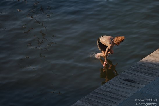A person with tattoos is jumping into a body of water from a wooden dock in Amsterdam, - image from year 2026 #003