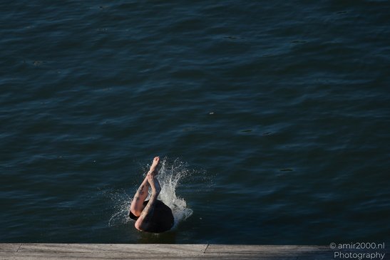 A person is diving into a body of water, creating a splash, with their legs and tattooed in - image from year 2026 #003