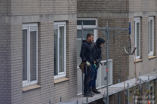 Two workers on a scaffolding platform in front of a brick building. - image from year 2026 #001