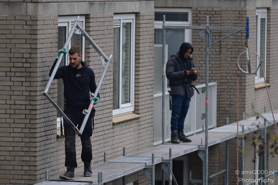Two workers on scaffolding, one using a tool and the other looking at his phone. - image from year 2026 #002