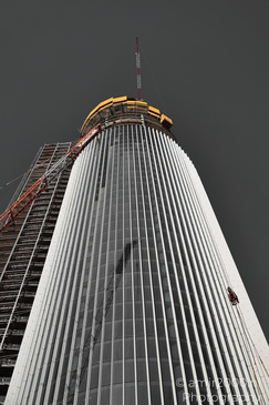 A tall skyscraper under construction with scaffolding on the left side and a dark sky in the - image from year 2026 #008