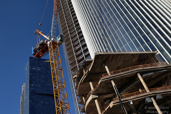 A yellow construction crane is positioned next to an unfinished skyscraper under clear blue - image from year 2026 #010