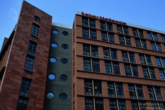 A modern office building with a distinctive red brick facade and circular windows. - image from year 2026 #001