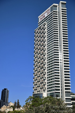 A tall residential building with numerous balconies under clear blue skies, surrounded by other - image from year 2026 #002