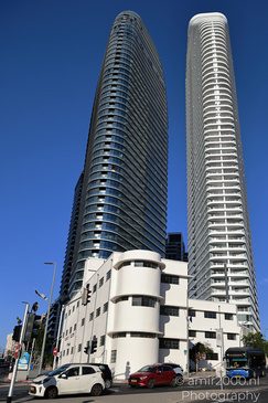 Two modern high rise buildings with curved facades positioned side by side against a clear blue - image from year 2026 #004
