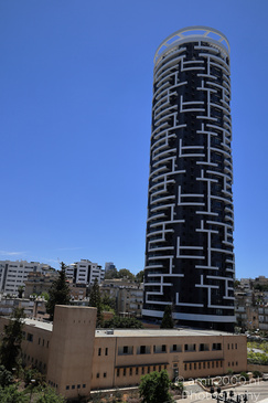 A tall, cylindrical building with a unique geometric pattern on its facade stands prominently - image from year 2026 #003