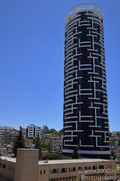 A tall, cylindrical building with a unique geometric pattern stands prominently against the blue - image from year 2026 #004