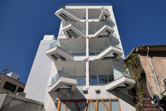 A modern white building with multiple levels of balconies and glass railings, situated against a - image from year 2026 #002