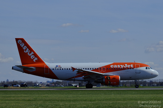 An EasyJet aircraft on a runway with grass and some distant structures in the background under a - image from year 2026 #003
