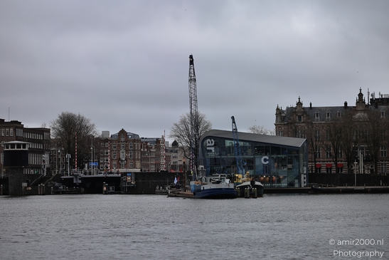 Waterfront scene including boat docked at pier, modern building labeled 'ARCAM', cloudy sky, trees image from year 2026 #1