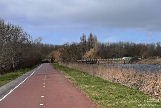 Red cycling track beside waterway with bare trees and cloudy sky. image from year 2026 #1