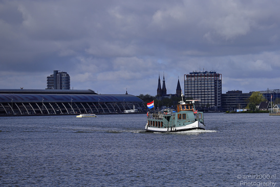 A boat sails on a calm river with a cityscape. - image from year 2026 #001