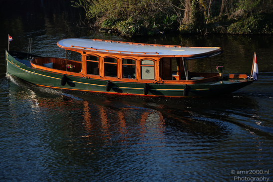 A vintage boat with a green hull and orange trim glides through calm water near lush greenery. - image from year 2026 #001