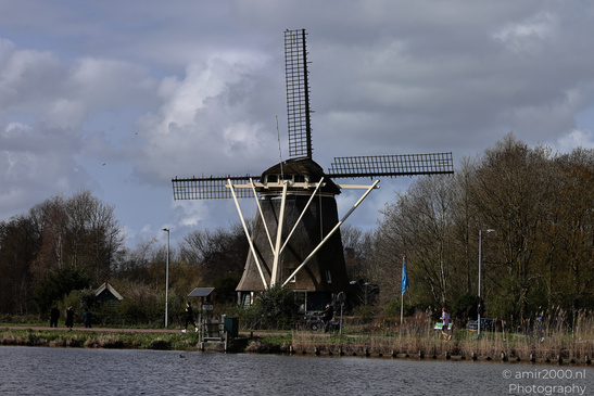 A traditional windmill stands by calm water under an overcast sky. - image from year 2026 #001