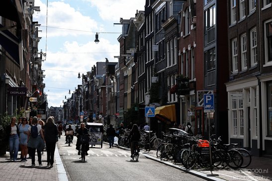 A street scene with pedestrians, cyclists, parked bicycles, and buildings lining both sides of - image from year 2026 #002