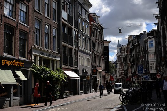 A street scene in Amsterdam with tall, narrow buildings on either side, shops with awnings, - image from year 2026 #006
