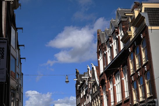 A row of buildings with brick facades and white trim, under a blue sky with scattered clouds in - image from year 2026 #007