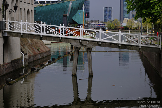 Canal with a white pedestrian bridge over calm water, reflecting the surrounding buildings and - image from year 2026 #001