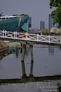 A bridge with white railings over a canal, reflecting its structure on the water's surface, with - image from year 2026 #002