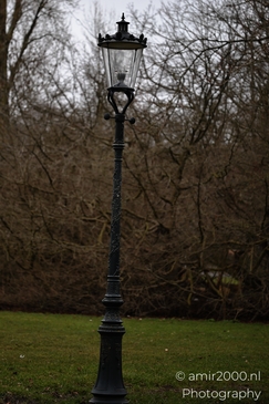 An ornate black metal streetlamp with glass panels and decorative details on grassy ground near image from year 2026 #2