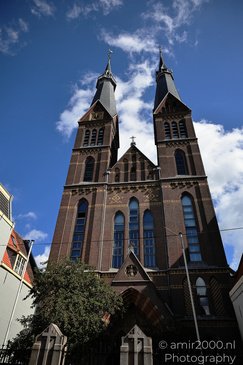 A church with two tall, pointed towers, a brick facade with arched windows, and a clear blue sky - image from year 2026 #001
