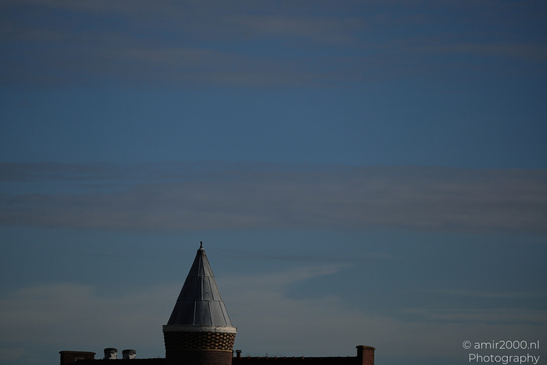 A clear sky with scattered clouds and part of a building featuring a pointed roof structure in - image from year 2026 #001