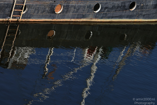A ships reflection in the water shows a ladder and circular openings. - image from year 2026 #001