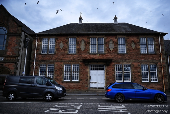 A black van and a blue car are parked in front of an old brick building with white windows. - image from year 2026 #015