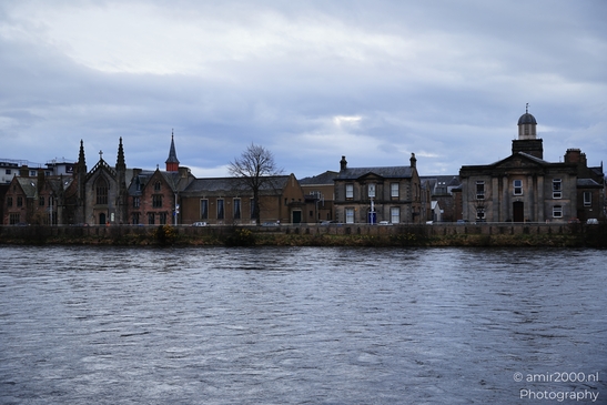 A Scottish cityscape with historic buildings along the riverbank under a cloudy sky. - image from year 2026 #022