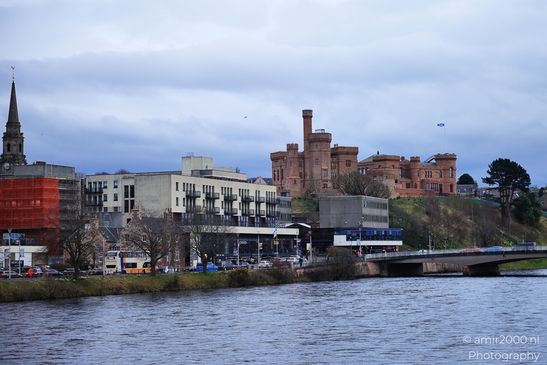 A riverside scene featuring a castle like building on a hill, surrounded by modern buildings and - image from year 2026 #027
